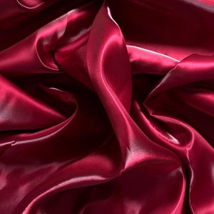 Peut inclure: Gros plan sur un tissu fluide de couleur bordeaux profond. Le matériau présente un aspect satiné soyeux, avec des plis et des reflets doux qui créent une sensation de profondeur et de mouvement. Le tissu semble lisse et élégant.