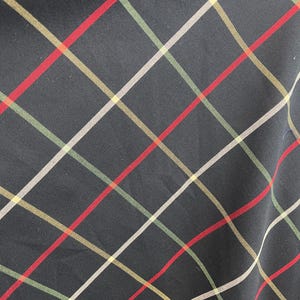 May include: Close-up of a black fabric with a plaid pattern. The plaid design features intersecting lines in red, white, green, and gold. The fabric has a slight sheen.