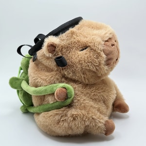 May include: A brown plush capybara with a green and black climbing chalk bag. The capybara is sitting with its legs crossed and its head tilted to the side.