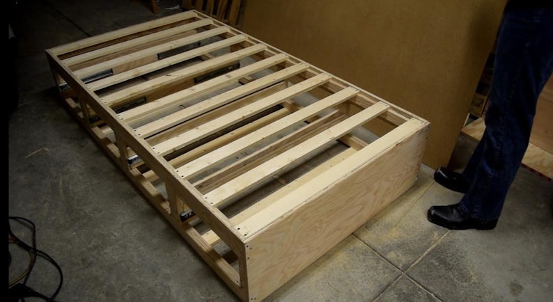 Puede incluir: Un marco de cama de madera con listones y un fondo de madera contrachapada. El marco est&aacute; sin terminar y tiene un color de madera natural.