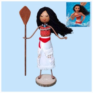 Pu&ograve; includere: Bambola fatta a mano di Moana del film d'animazione Disney Moana, con lunghi capelli neri, un top rosso, una gonna bianca e una pagaia di legno marrone.