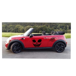 Könnte beinhalten: Ein rotes Cabriolet mit einem schwarzen Totenkopf- und Krallen-Aufkleber an der Seite.