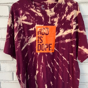 May include: A maroon tie-dye t-shirt with an orange square graphic that says "GOD IS DOPE."