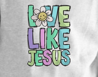 Könnte beinhalten: Ein hellgraues Sweatshirt mit dem gestickten Text "LOVE LIKE JESUS" in einer farbenfrohen, genähten Schriftart. Das Wort "LOVE" zeigt eine Gänseblümchen mit einem lächelnden Gesicht. Die Buchstaben sind schwarz umrandet.