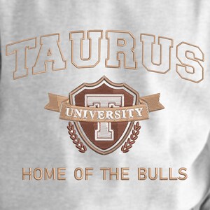 May include: White sweatshirt with brown embroidered text "TAURUS UNIVERSITY" and a shield with a "T" inside. Below the shield is the text "HOME OF THE BULLS".