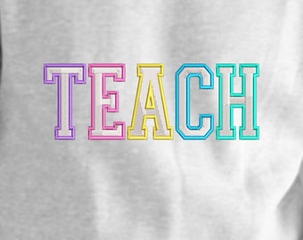 May include: A white sweatshirt with the word "TEACH" embroidered in colorful letters. The letters are outlined in white and each letter is a different color: purple, pink, yellow, blue, and turquoise.