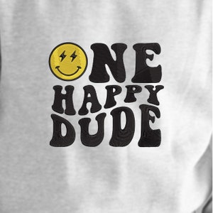 Pode incluir: Uma camisa de moletom branca com texto bordado em preto que diz "One Happy Dude" e um rosto sorridente amarelo com raios para os olhos.