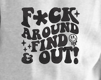 May include: A light gray sweatshirt with black embroidered text that reads "F*CK AROUND FIND OUT!" in a retro font. The design includes stars and a melting smiley face.