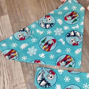 May include: Two turquoise dog bandanas with a repeating pattern of Jack Skellington and Sally from The Nightmare Before Christmas, snowflakes, and bats. The characters are in circular frames. The bandanas are triangular.