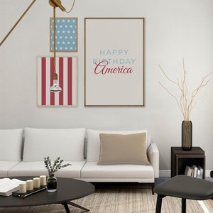 Pode incluir: Um sof&aacute; branco com uma almofada bege numa sala de estar com uma mesa de centro preta e uma cadeira preta. H&aacute; tr&ecirc;s impress&otilde;es emolduradas na parede atr&aacute;s do sof&aacute;. A impress&atilde;o central diz "Happy Birthday America".
