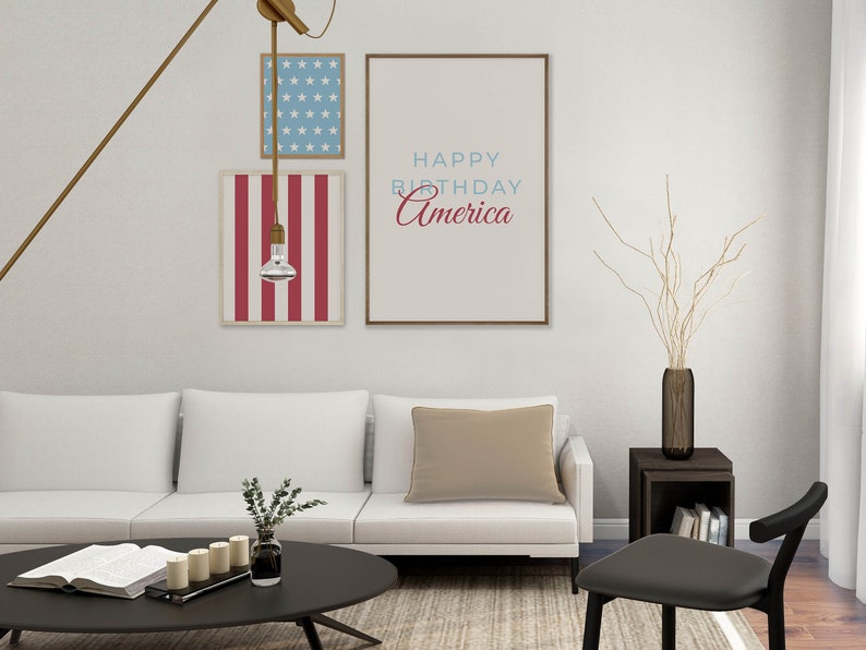 Pode incluir: Um sof&aacute; branco com uma almofada bege numa sala de estar com uma mesa de centro preta e uma cadeira preta. H&aacute; tr&ecirc;s impress&otilde;es emolduradas na parede atr&aacute;s do sof&aacute;. A impress&atilde;o central diz "Happy Birthday America".