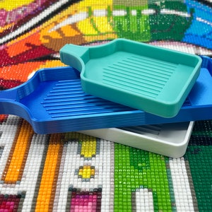 May include: Three diamond painting trays stacked on top of each other. The top tray is light blue, the middle tray is blue, and the bottom tray is white.