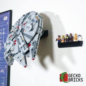 May include: A white and grey Lego Millennium Falcon spaceship model mounted on a black wall mount. A group of Lego minifigures are displayed on a black shelf below the spaceship. The text "Gecko Bricks" is visible in the lower right corner of the image.
