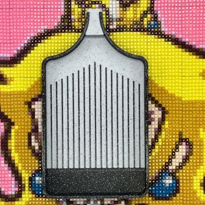 May include: A grey diamond painting tool with a black handle and a grid of small metal prongs. The tool is used to pick up and place diamonds on a diamond painting canvas.