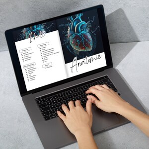 Op de afbeelding: Een laptop met een zwart scherm waarop een document wordt weergegeven met het woord "Inhalt" en een 3D-afbeelding van een menselijk hart. Het document bevat ook een lijst met onderwerpen, waaronder "Anatomie" en "Physiologie". De laptop staat op een grijs oppervlak en de handen van een persoon typen op het toetsenbord.