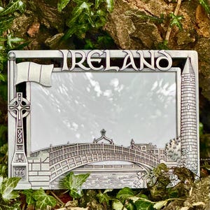 May include: A silver metal picture frame with an embossed image of a bridge and the word "IRELAND" on the top. The frame is designed to hold a 4x6 inch photo.