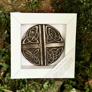 Könnte beinhalten: Ein keltisches Liebeskreuz in einem weißen Rahmen mit einem bronzefarbenen Metalldesign. Die Inschrift lautet: "Liebe allein ist in der Lage, Menschen so zu vereinen, dass sie sich vervollständigen und erfüllen, denn sie nimmt sie und verbindet sie durch das, was in ihnen am tiefsten ist."