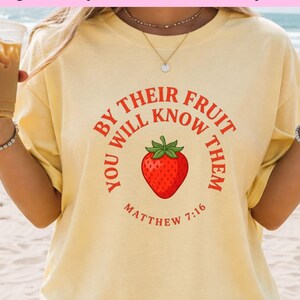 Peut inclure: T-shirt jaune clair avec une fraise rouge et l'inscription « You Will Know Them By Their Fruit » et « Matthew 7:16 ». Le t-shirt contient également le texte « High-Quality Files: PNG, and PDF formats » et « Instant Download: No waiting, start your project right away! »
