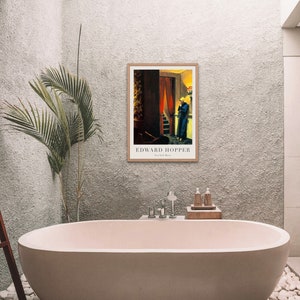 May include: A framed print of a painting by Edward Hopper titled "Room in New York". The painting depicts a woman in a blue dress standing in a doorway with a red curtain.