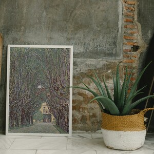 May include: A framed print of a painting depicting a tree-lined path leading to a building in the distance. The painting is in a muted color palette of greens, purples, and browns. The print is hanging on a wall with a rustic texture.