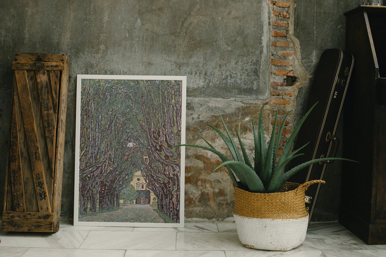 May include: A framed print of a painting depicting a tree-lined path leading to a building in the distance. The painting is in a muted color palette of greens, purples, and browns. The print is hanging on a wall with a rustic texture.