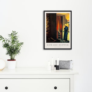 May include: A framed poster of a painting by Edward Hopper titled "New York Movie". The painting depicts a woman in a blue dress standing in a doorway with a red curtain. The woman is looking down at something in her hand.