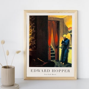 May include: A framed print of a painting by Edward Hopper titled "New York Movie". The painting depicts a woman in a blue dress standing in a dimly lit hallway with a red curtain and a staircase.