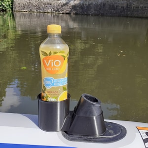 Könnte beinhalten: Ein schwarzer Getränkehalter mit einer Flasche Vio Bio Limo Orangensaft drin. Der Halter ist an einem weißen Schlauchboot befestigt.