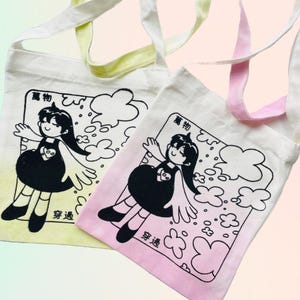 Puede incluir: Dos bolsas de tela con una ilustración en blanco y negro de una niña con alas. La niña lleva un vestido y tiene un corazón en el pecho. El texto "宝物" y "夢追" está impreso en las bolsas. Las bolsas están teñidas en amarillo y rosa.