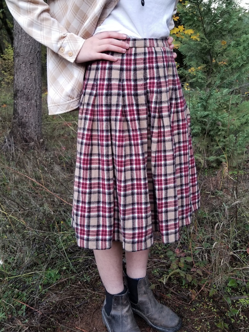 May include: A brown, red, and white plaid skirt with pleats. The skirt is knee-length and has a fitted waist.