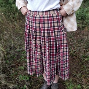 May include: A red, black, and beige plaid pleated skirt with a button closure. The skirt is knee-length and has a relaxed fit.