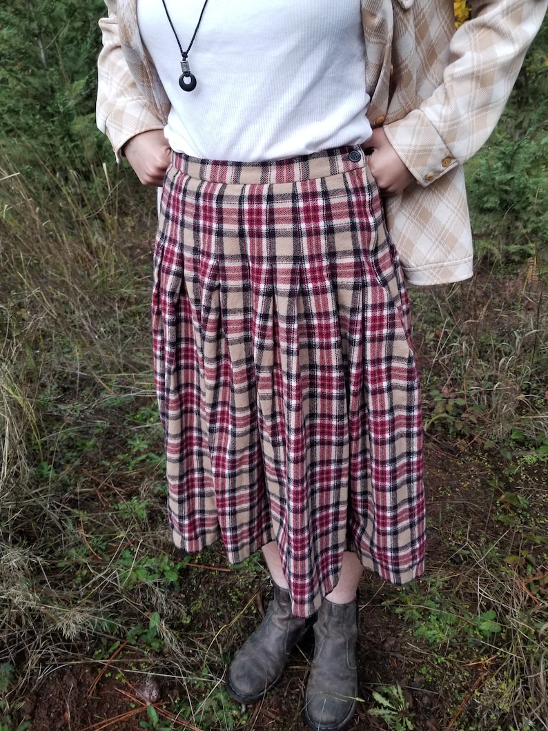 May include: A red, black, and beige plaid pleated skirt with a button closure. The skirt is knee-length and has a relaxed fit.