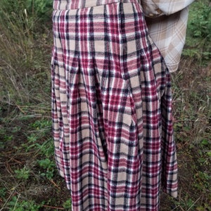 May include: A red, black, and beige plaid skirt with pleats. The skirt is knee-length and has a button closure at the waist.