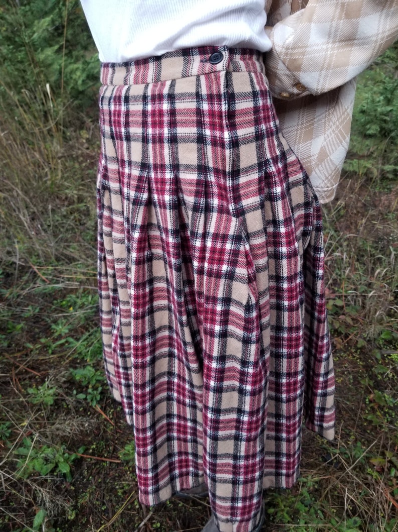 May include: A red, black, and beige plaid skirt with pleats. The skirt is knee-length and has a button closure at the waist.