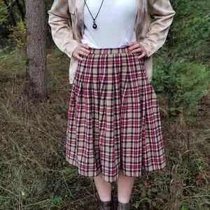 May include: A plaid skirt with a brown, red, and black pattern. The skirt is pleated and falls to the knee. The skirt is paired with a white t-shirt and a beige plaid shirt.