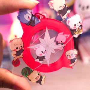 May include: A red and clear acrylic charm with a star design and seven cartoon animal figures. The animals are a pink bunny, a white bunny, a brown bunny, a pink pig, a white dog, a brown dog, and a blue dog. The charm is attached to a silver chain.