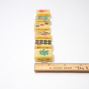 May include: A row of vintage yellow Mahjong tiles with various symbols in red, green, and black. A wooden ruler with the text "A Good Rule Do Unto Others" is next to the tiles. The tiles are rectangular and have a slightly translucent appearance.