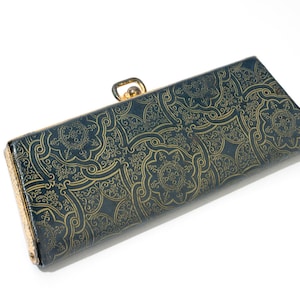 May include: A rectangular clutch with a dark blue background and a gold floral pattern. The clutch has a gold clasp and a gold trim on the sides. The clutch is closed and is on a white background.