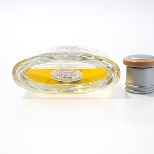 May include: An oval-shaped glass cologne bottle with a silver cap and a wooden ring. The bottle contains a yellow liquid and has a label that reads "Stetson Country Cologne Spray 2.5 FL OZ 75 ml".