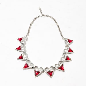 Könnte beinhalten: Eine silberne Halskette mit einer Kette und roten dreieckigen Anhängern.