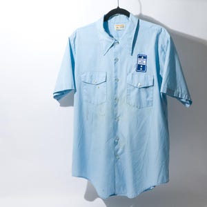 May include: A light blue short-sleeved button-down shirt with a patch on the left chest that says "Southern Bell Telephone Co."