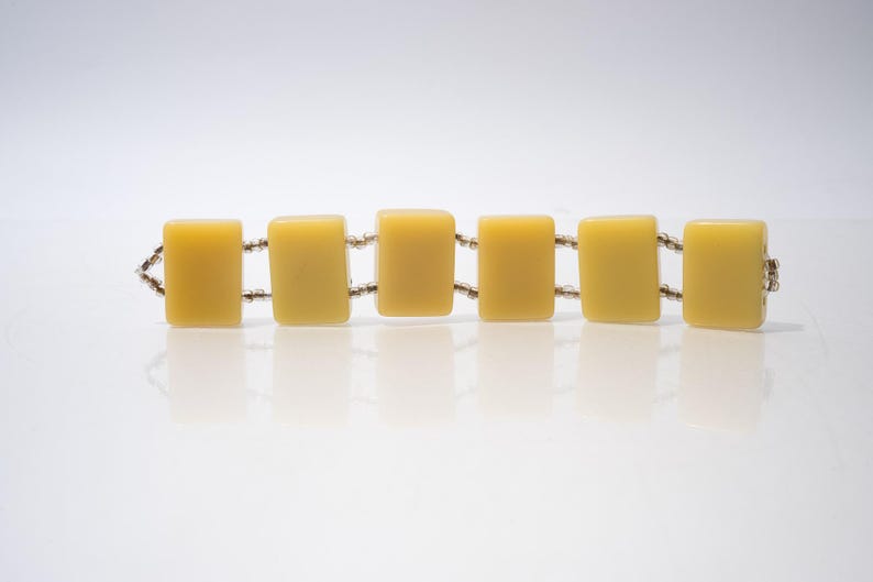May include: A vintage bracelet featuring six rectangular, yellow-toned beads connected by small, silver-colored links. The bracelet is displayed on a white surface, showcasing its simple yet elegant design. The beads have a smooth, polished appearance.