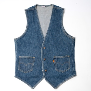 May include: A blue denim vest featuring a V-neckline, a three-button front closure, and two patch pockets on the lower front. The vest includes a small orange tab on the right pocket and a light gray interior lining, showcasing a classic sleeveless design.