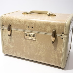 May include: A vintage Samsonite suitcase in a beige color with a textured finish. The suitcase has a handle, metal latches, and a combination lock. The corners and edges are trimmed in a lighter beige color.