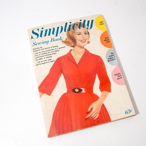 May include: Vintage "Simplicity Sewing Book" cover featuring a woman in a red dress. The book has a white background with the title in blue and the price 65¢. The cover also includes text about sewing techniques.