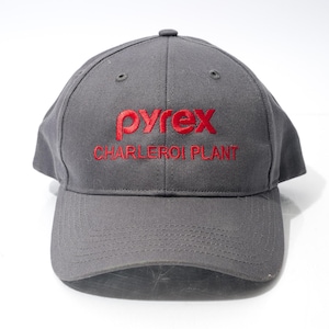 May include: A gray baseball cap with the word "pyrex" in red embroidered lettering. Below the word "pyrex" is the text "CHARLEROI PLANT" in red. The cap has a curved brim and a button on top.