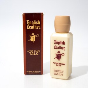 May include: An off-white bottle of English Leather after-shave talc with a tan cap and a brown box. The box and bottle feature the English Leather logo and a saddle illustration. The bottle contains 93.5 grams of talc.