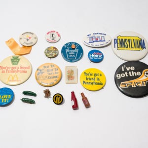 May include: A collection of vintage buttons featuring various designs and slogans, including "You've got a friend in Pennsylvania", "I've got the spirit", and "Keystone Area Local".