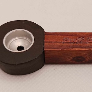 Puede incluir: Una pipa de fumar de madera con una cazoleta negra y un inserto de metal plateado. La pipa está grabada con las palabras "Puff Puff Pass".