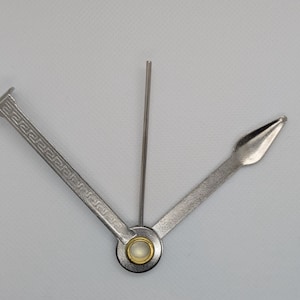 Puede incluir: Una herramienta de pipa de metal plateado con tres componentes: un limpiador, un escariador y un pisón. El pisón tiene un patrón decorativo. La herramienta está diseñada para el mantenimiento y la limpieza de pipas.